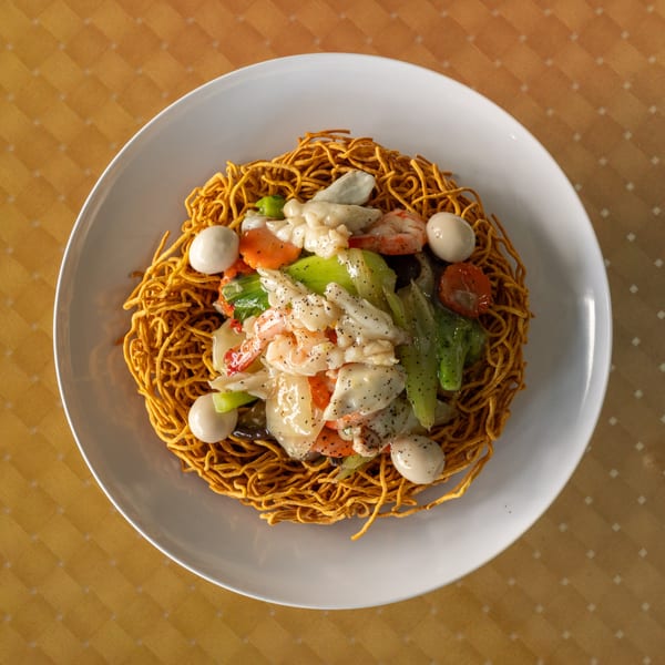 Crispy noodles topped with shrimp, squid, vegetables, and quail eggs in a white sauce.