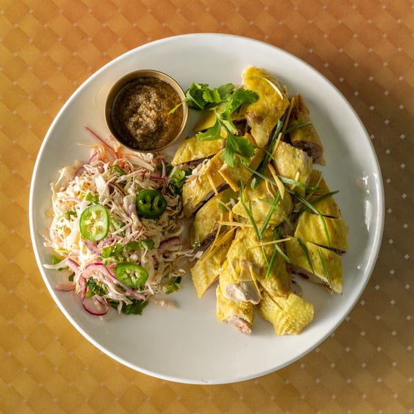 Hainanese chicken, a side salad with jalapeños, and a small bowl of sauce on a white plate.