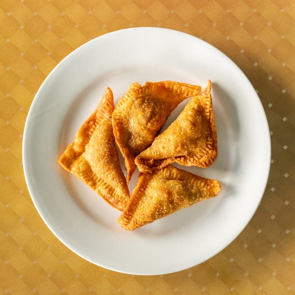 Four golden-brown, triangular fried dumplings with crimped edges, served on a white plate.