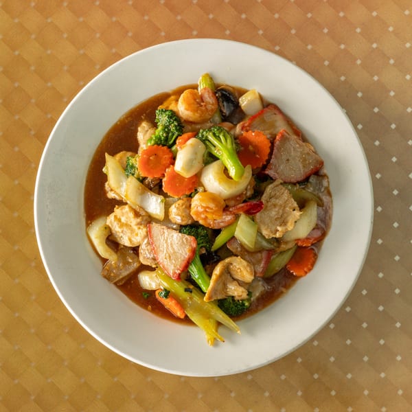 A white plate filled with a colorful stir-fry of meat, shrimp, broccoli, carrots, and onions in sauce.