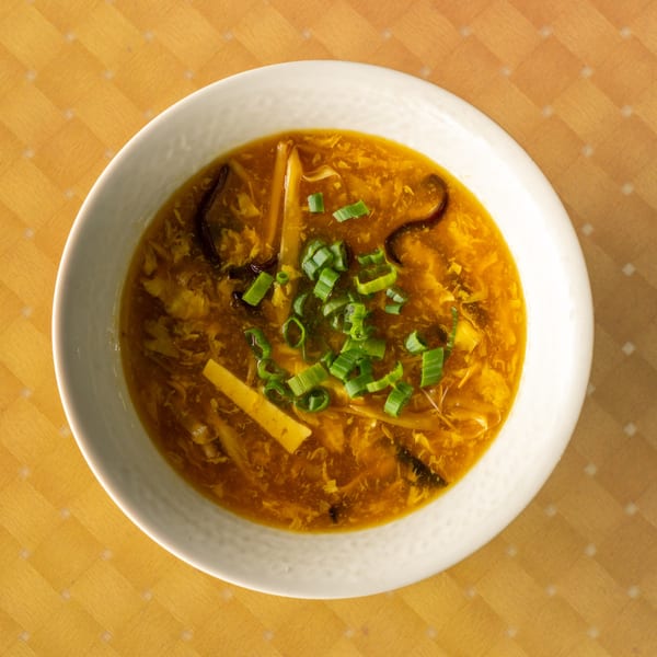 Hot and sour soup in a white bowl, garnished with green onions, on a wooden table.