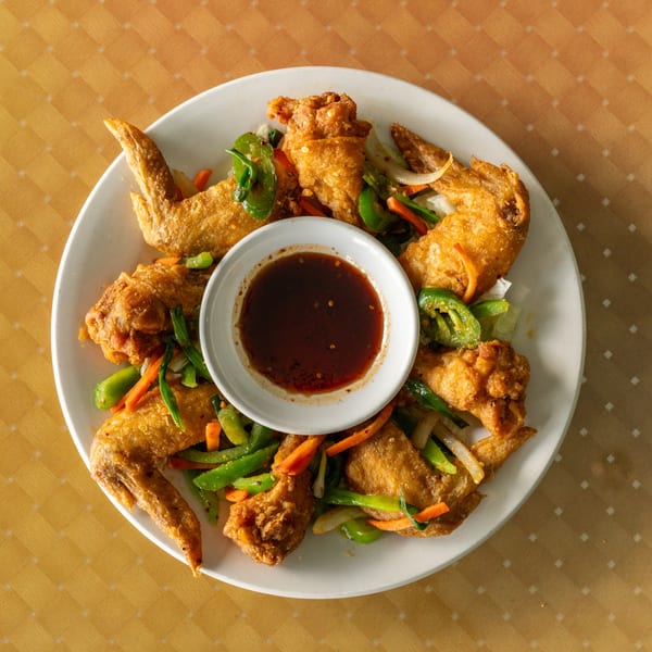 Crispy fried chicken wings with green peppers, carrots, onions, and a dark dipping sauce.