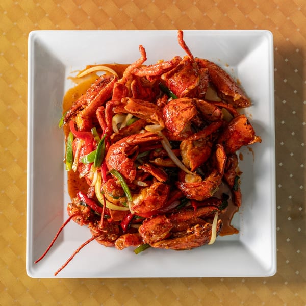 Spicy lobster stir-fry with red peppers, green onions, and white onions on a white plate.